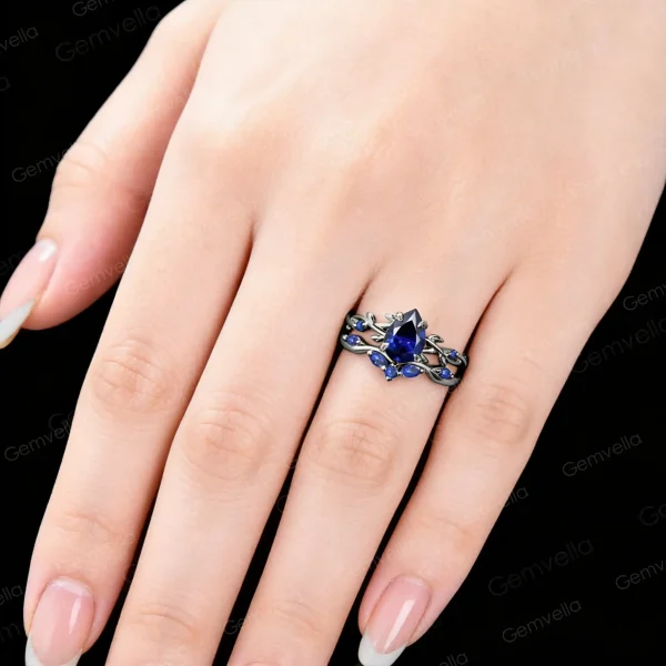 Close up shot of the black gold 1.25ct pear cut blue sapphire ring set worn on a woman's hand, displaying how the gothic twig vine engagement and wedding rings look when worn.
