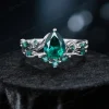 A front view of a vintage-inspired engagement ring set featuring pear-shaped emeralds and intricate twig vine detailing.