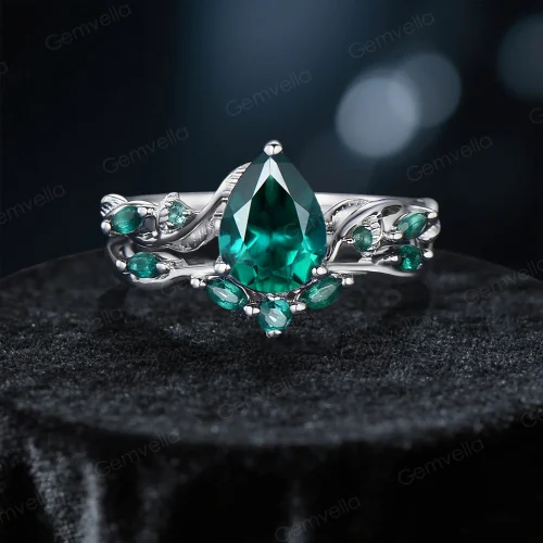 A front view of a vintage-inspired engagement ring set featuring pear-shaped emeralds and intricate twig vine detailing.