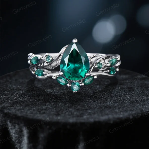 A front view of a vintage-inspired engagement ring set featuring pear-shaped emeralds and intricate twig vine detailing.
