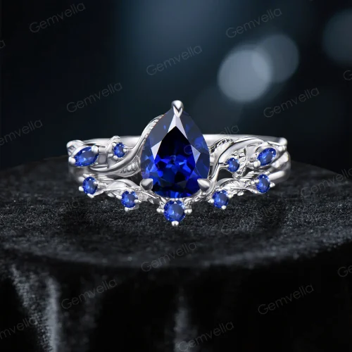 Front view of a 1.25ct pear-cut blue sapphire engagement ring and matching wedding band, crafted in sterling silver with a detailed twig vine and leaf nature-inspired design, showcasing the central gemstone and intricate metalwork.