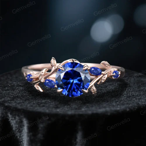 Front view of a vintage-inspired engagement ring featuring a round blue sapphire center stone, encircled by a delicate rose gold leaf and vine band.