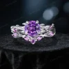 Frontal view of a nature-inspired bridal ring set featuring a deep purple round cut Amethyst center stone, surrounded by an intricate sterling silver twisting vine and leaf setting paved with smaller sparkling Amethyst gems.