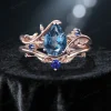 Front view of 1.25ct natural London blue topaz engagement ring set, featuring a pear-shaped blue topaz center stone surrounded by blue sapphire accents and rose gold leaf-branch detailing.