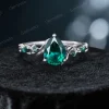 A close-up front view of the main ring in the set, featuring a prominent pear-shaped emerald center stone and nature-inspired twig vine details.
