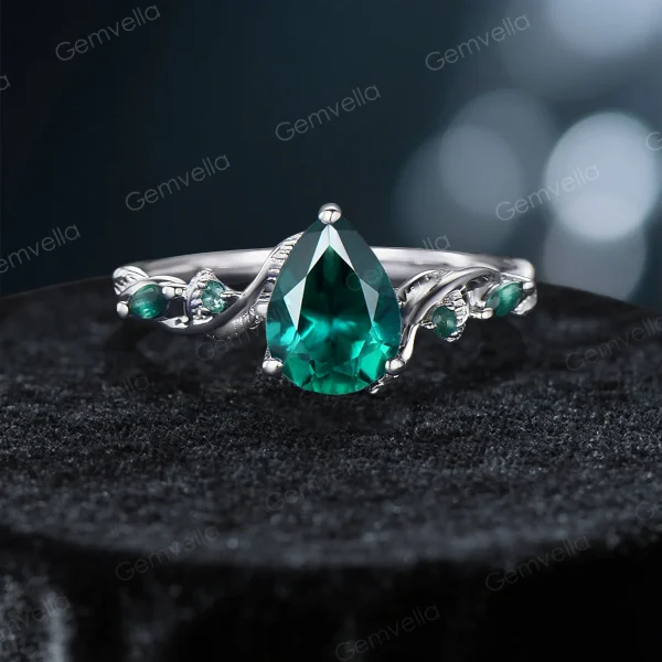 A close-up front view of the main ring in the set, featuring a prominent pear-shaped emerald center stone and nature-inspired twig vine details.