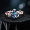 Detailed front view of the 1.25ct natural London blue topaz engagement ring, focusing on the pear-shaped blue topaz, blue sapphire side stones, and the delicate rose gold leaf-branch setting.