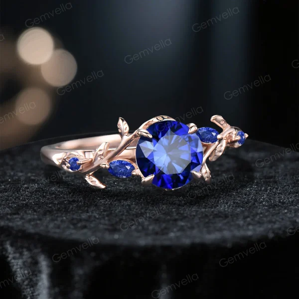A 45-degree angled shot of the rose gold sapphire ring, highlighting the relationship between the round blue gemstone and the nature-inspired leaf vine details on the band.